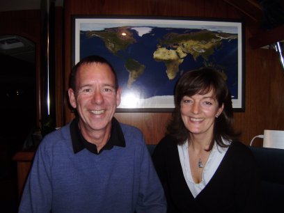 Chris & Sandra Mennem voor de wereldkaart in de salon van Deep Blue. Achter die kaart zit een breedbeeld televisie
