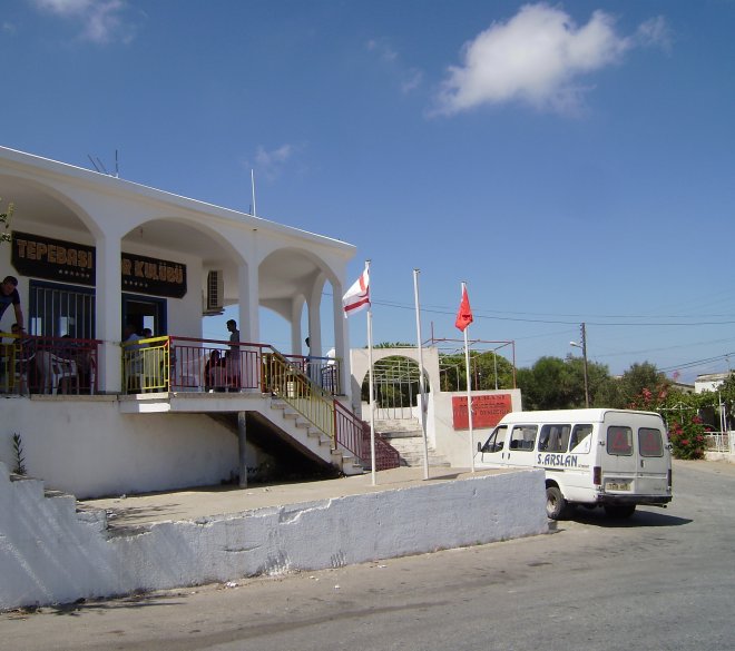 Verdwaald in het dorp Terebasi. We zitten op het terras van de kantine links. Zoals overal ernaast een Turkse en een Turks/Cyprische vlag. rechts het mini-busje