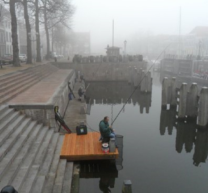 Zondagochtend met nevel. Drie vissers op de steiger beneden