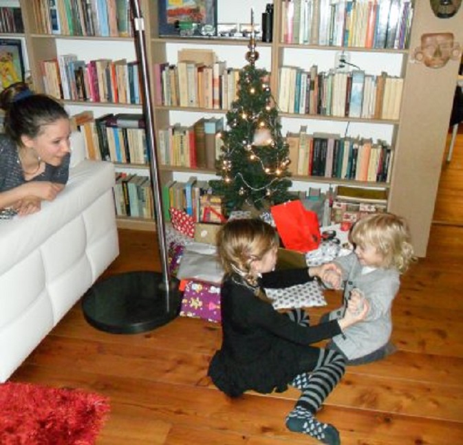 Esri en Caelan zingen een kerstliedje. Zometeen mogen ze cadeautjes van onder de kerstboom verdelen. Nikita (l) kijkt toe