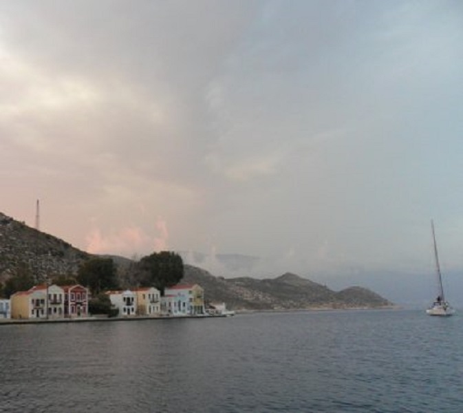 Kastellorizo. Boven de huisjes zie je opstijgende, witte wolkflarden, net horentjes. Er is een onweer in de maak
