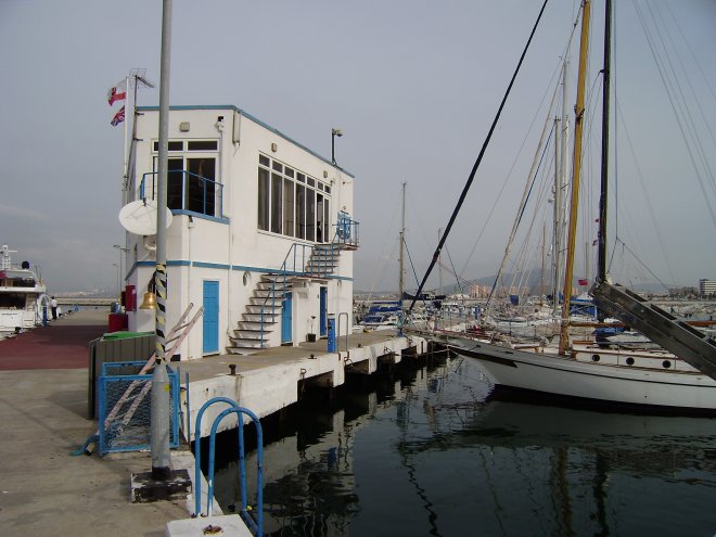 Onze haven Marina Bay in Gibraltar Het havenkantoor is op de bovenste verdieping van het gebouwtje. Vaag in de verte de bergen van Spanje.