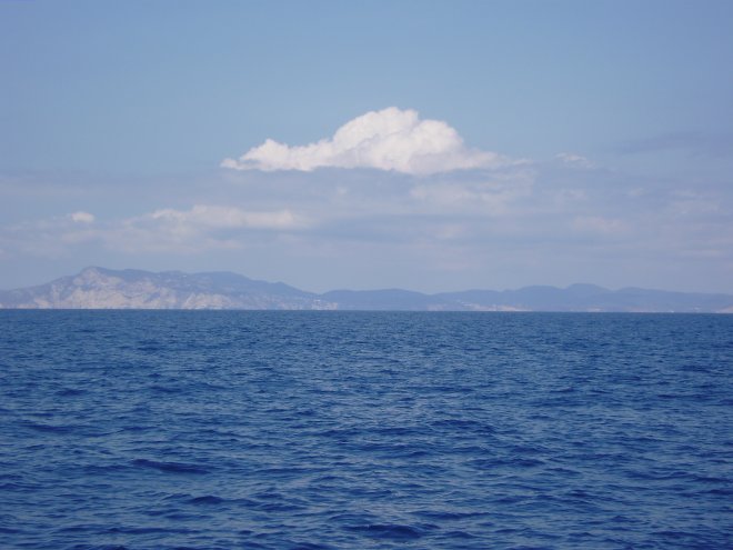 Op weg naar Formentera over een diepblauwe zee. In de verte hangt boven Ibiza een cumuluswolk. Teken van land.